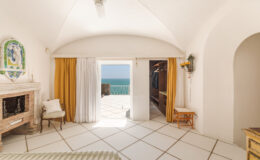 Bright and airy hotel room with white walls and tiled floor, featuring large windows with ocean views, elegant furnishings, and stylish decor. Perfect for a coastal getaway.