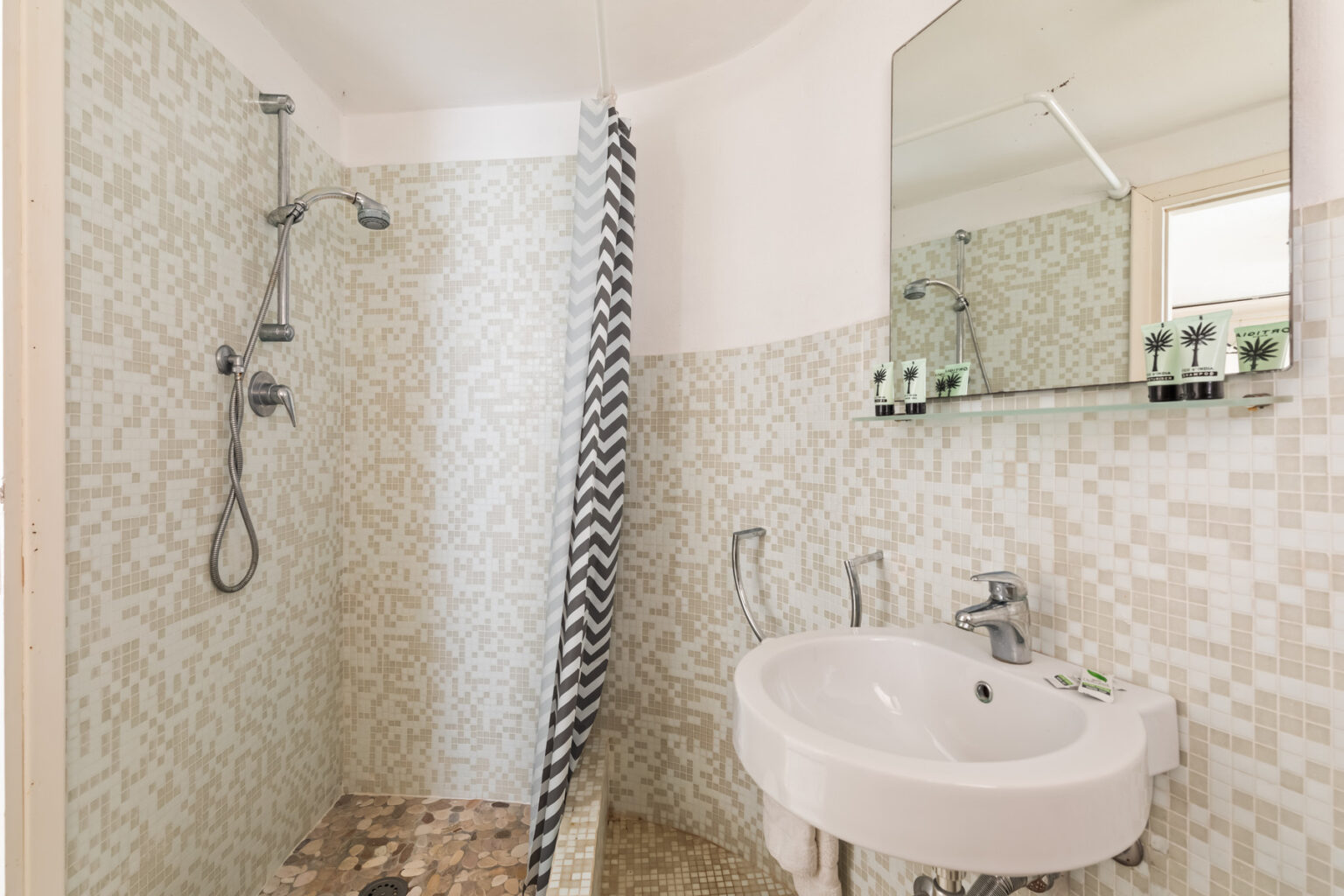Modern bathroom design featuring a walk-in shower with a sleek glass divider, a round vanity sink, and a large mirror. The walls are adorned with stylish mosaic tiles in neutral tones, creating a clean and contemporary aesthetic. | Only on SopranoVillas
