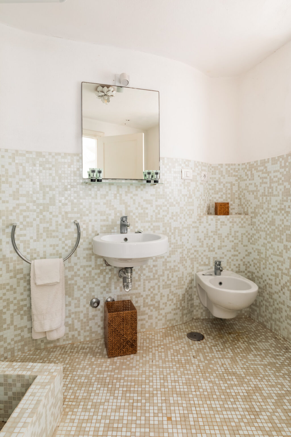 Modern bathroom featuring a wall-mounted sink, bidet, and a large mirror, with a light-colored mosaic tile design and minimalistic decor. | Only on SopranoVillas