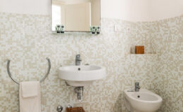 Modern bathroom featuring a wall-mounted sink, bidet, and a large mirror, with a light-colored mosaic tile design and minimalistic decor.