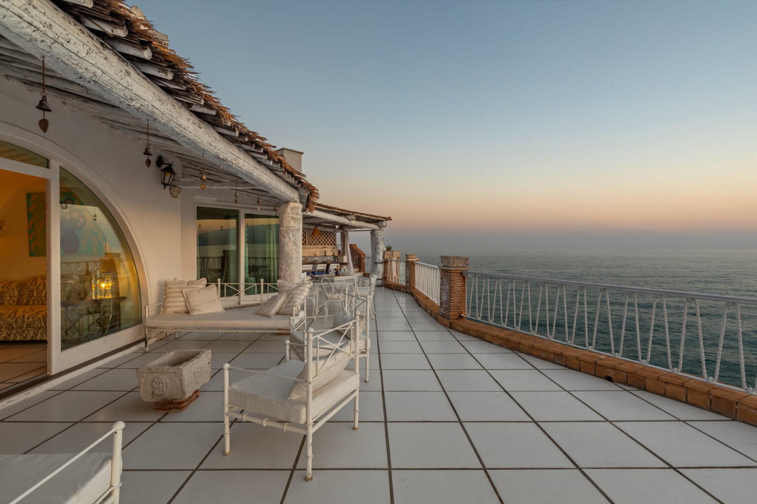 Cozy terrace overlooking the ocean at sunset, featuring white outdoor furniture and a modern design, perfect for relaxation and enjoying scenic views. | Only on SopranoVillas