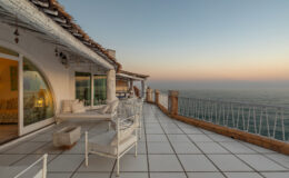 Cozy terrace overlooking the ocean at sunset, featuring white outdoor furniture and a modern design, perfect for relaxation and enjoying scenic views.