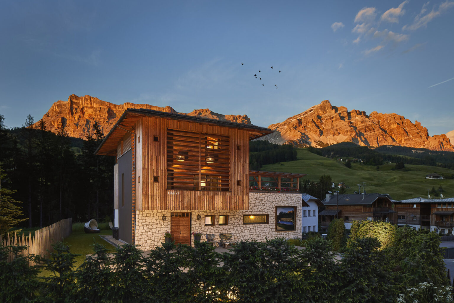 Modern wooden house surrounded by lush greenery and mountains at sunset, showcasing architectural design and natural beauty in a tranquil setting. | Only on SopranoVillas