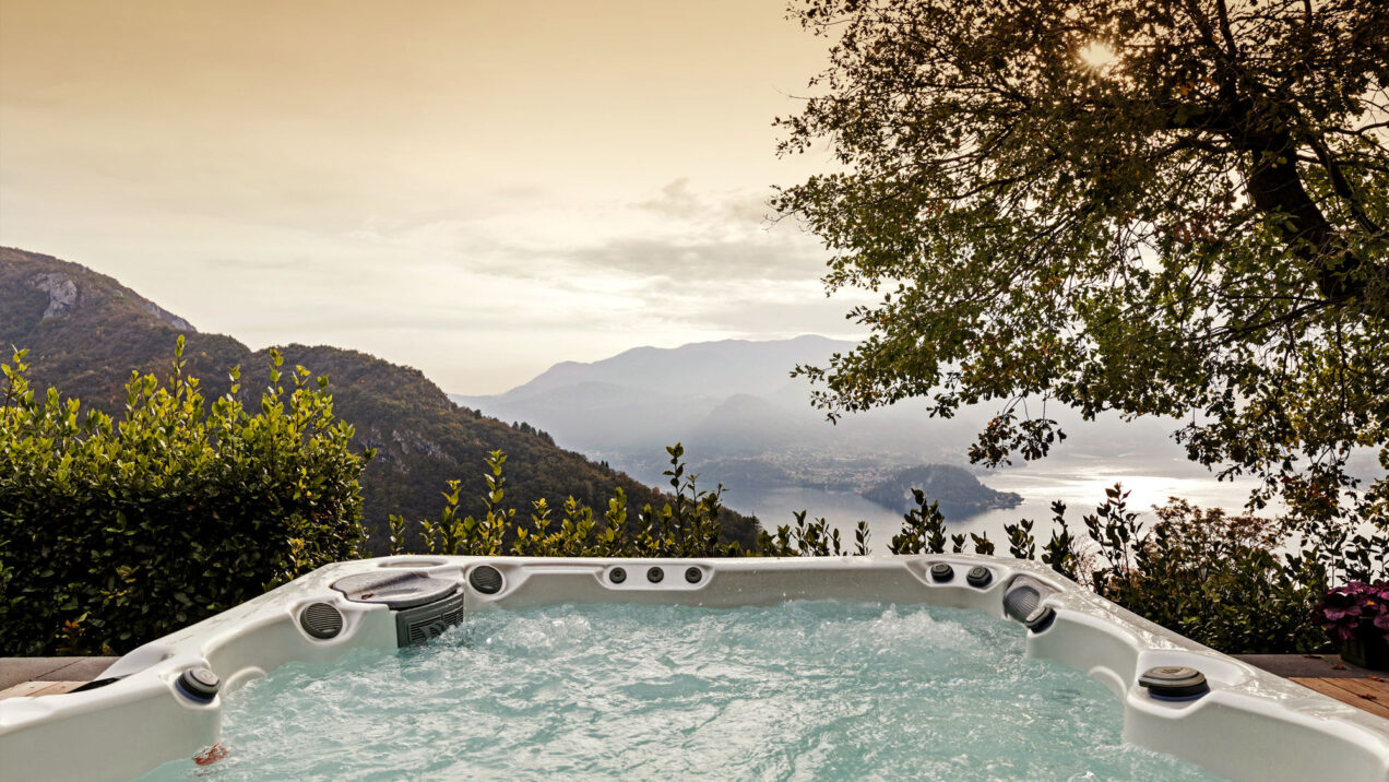 Hot tub overlooking a scenic mountain landscape at sunset, surrounded by lush greenery and tranquil waters. Perfect for relaxation and outdoor enjoyment.