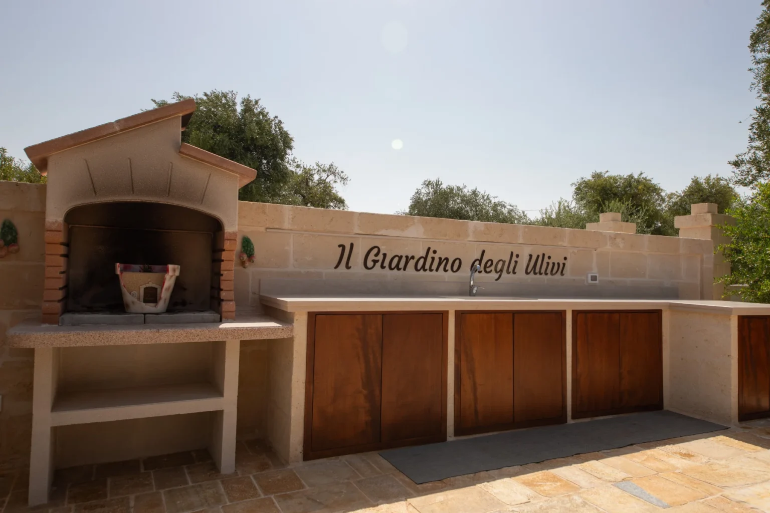 Outdoor kitchen area featuring a traditional stone pizza oven and a countertop with wooden cabinets, surrounded by olive trees, at Il Giardino degli Ulivi. | Only on SopranoVillas