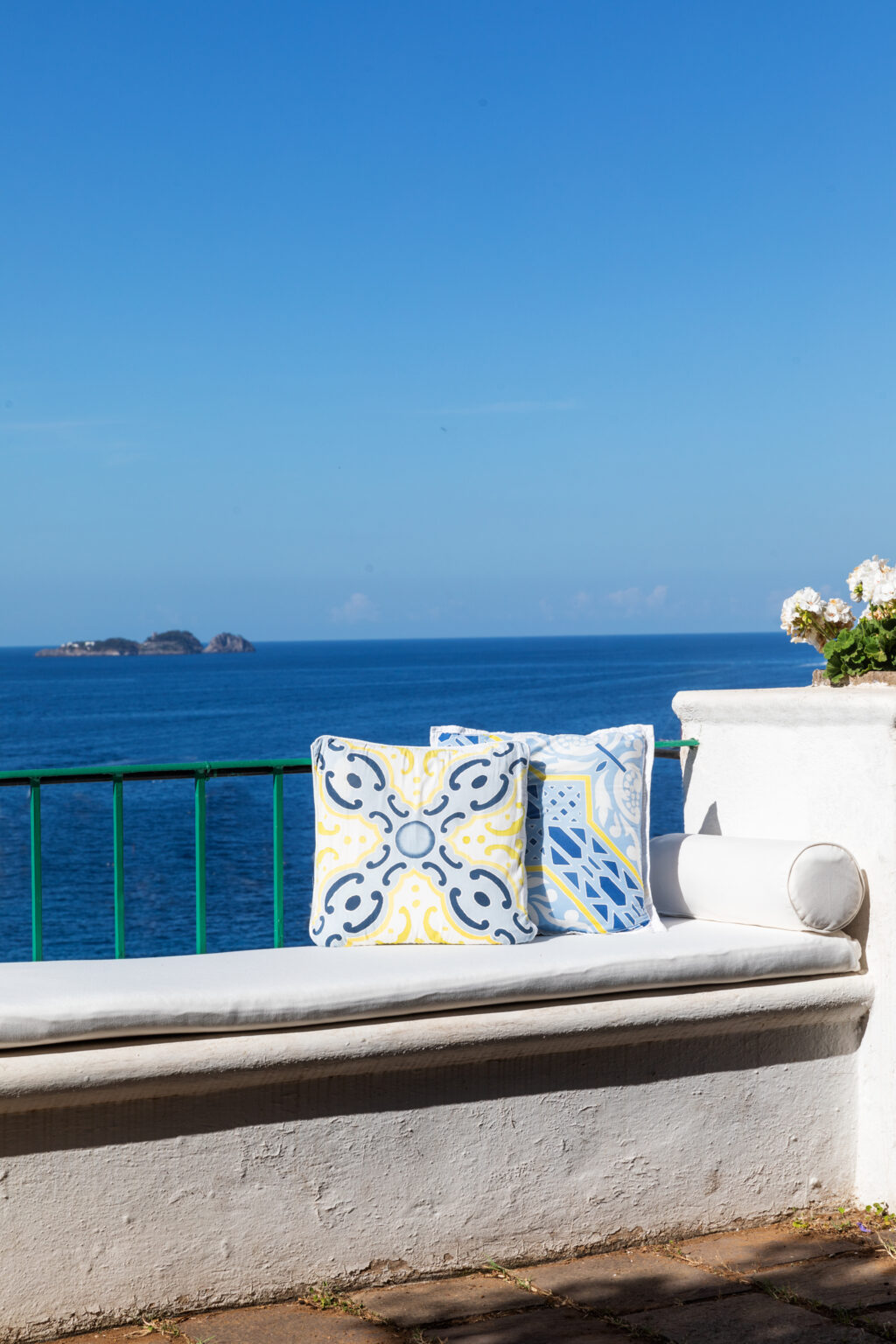 Colorful decorative pillows on a white terrace overlooking a serene blue ocean and distant islands, showcasing a tranquil coastal getaway. | Only on SopranoVillas
