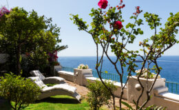 Lush garden with vibrant flowers, two lounge chairs, and a stunning ocean view under a clear blue sky, perfect for relaxation and outdoor enjoyment.