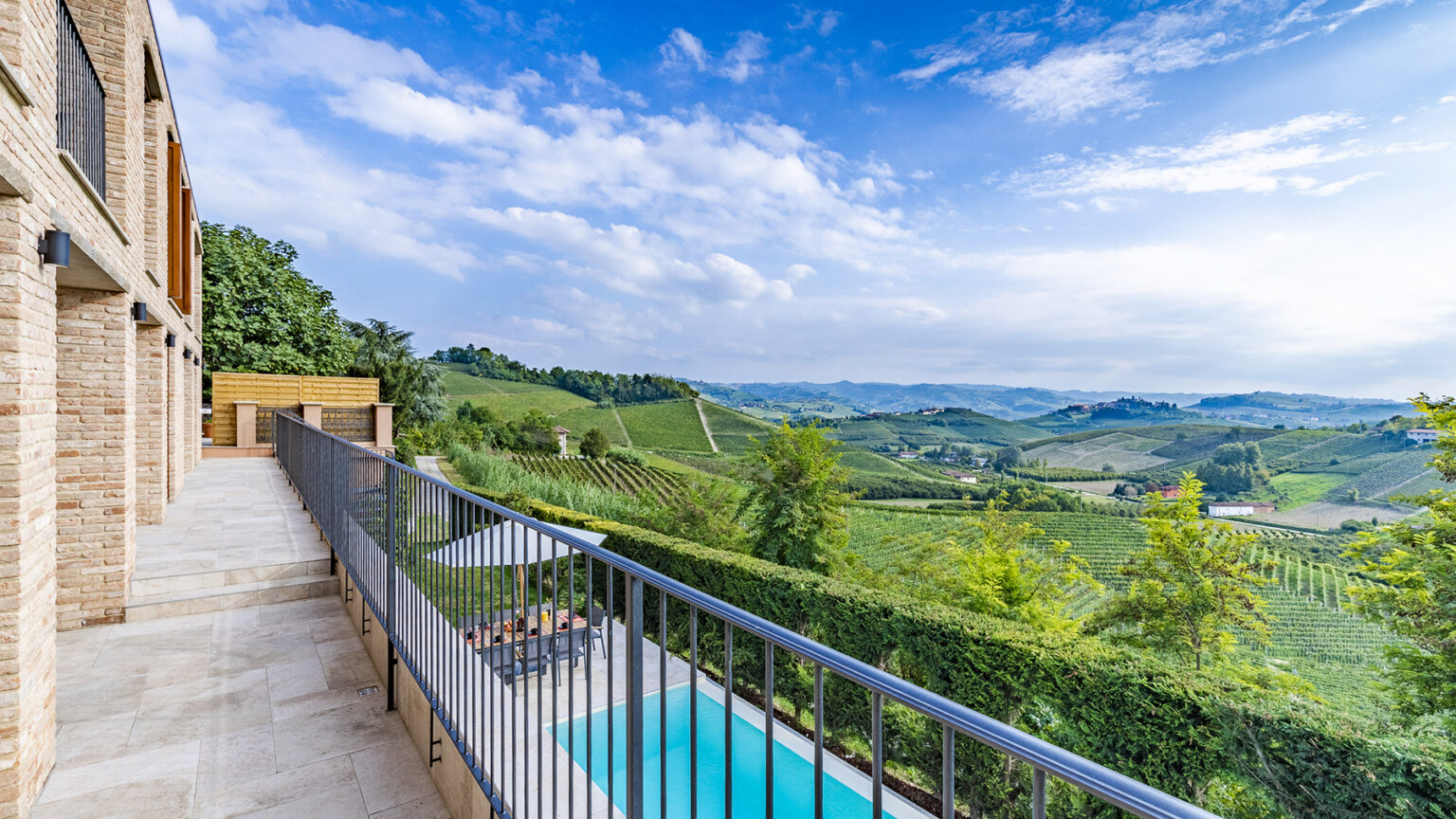 Scenic view from a balcony overlooking lush vineyards and a swimming pool, with a clear blue sky and rolling hills in the background. | Only on SopranoVillas