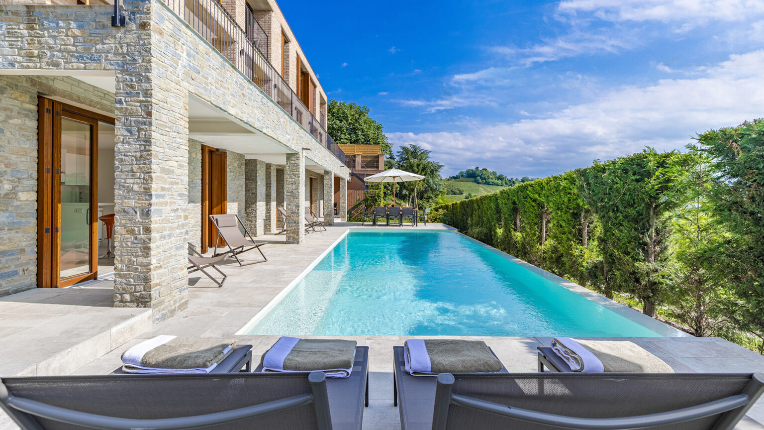 Luxury villa with a modern design featuring a private pool, loungers, and landscaped gardens under a clear blue sky. Perfect for relaxation and outdoor living. | Only on SopranoVillas