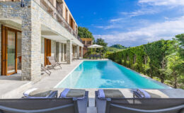 Luxury villa with a modern design featuring a private pool, loungers, and landscaped gardens under a clear blue sky. Perfect for relaxation and outdoor living.