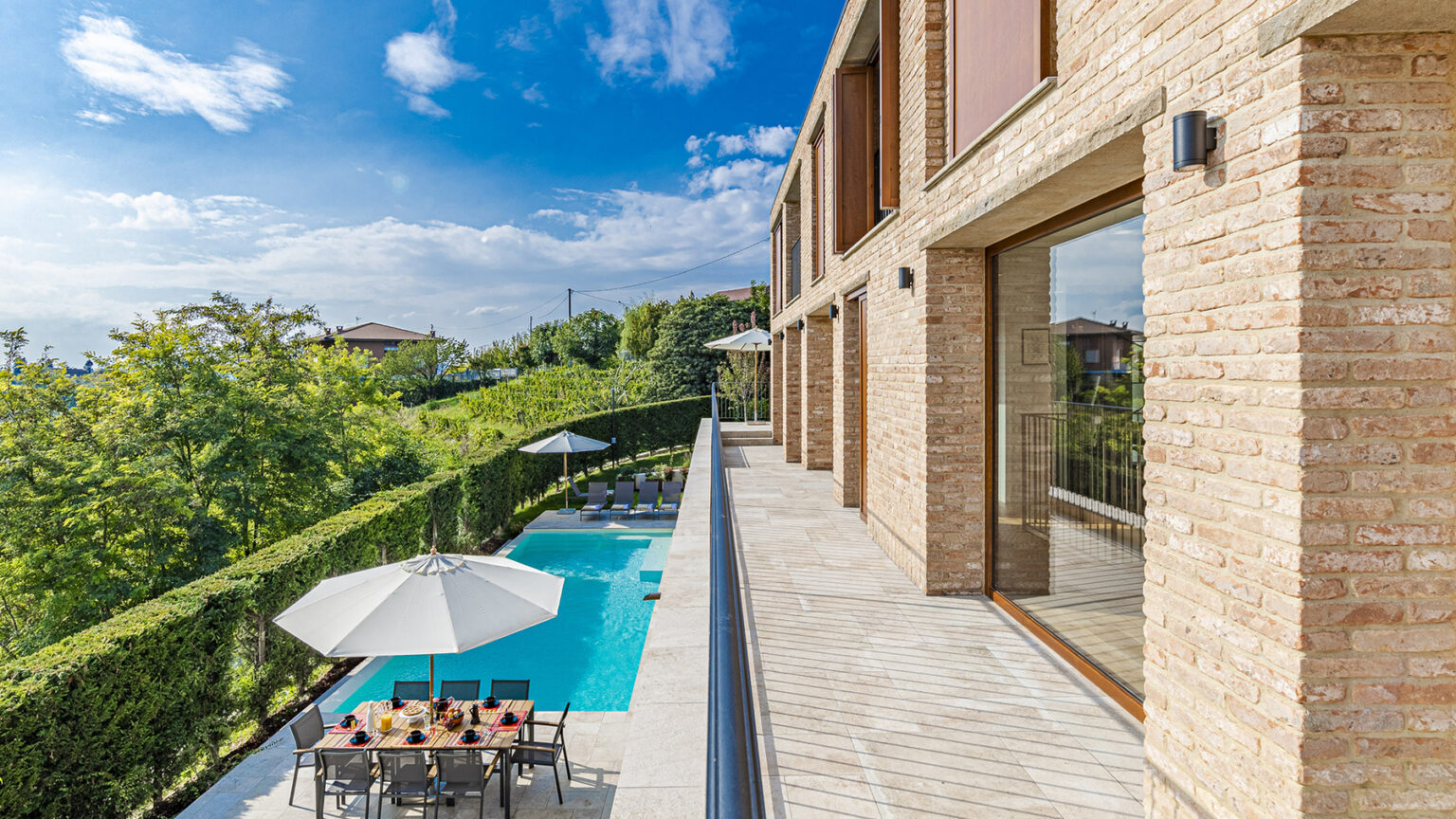 Modern villa exterior with a swimming pool, patio furniture, and lush greenery under a clear blue sky. Ideal for luxury living and outdoor relaxation. | Only on SopranoVillas