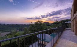 Scenic view from a balcony overlooking lush vineyards at sunset, with a tranquil sky and modern architecture in the foreground.