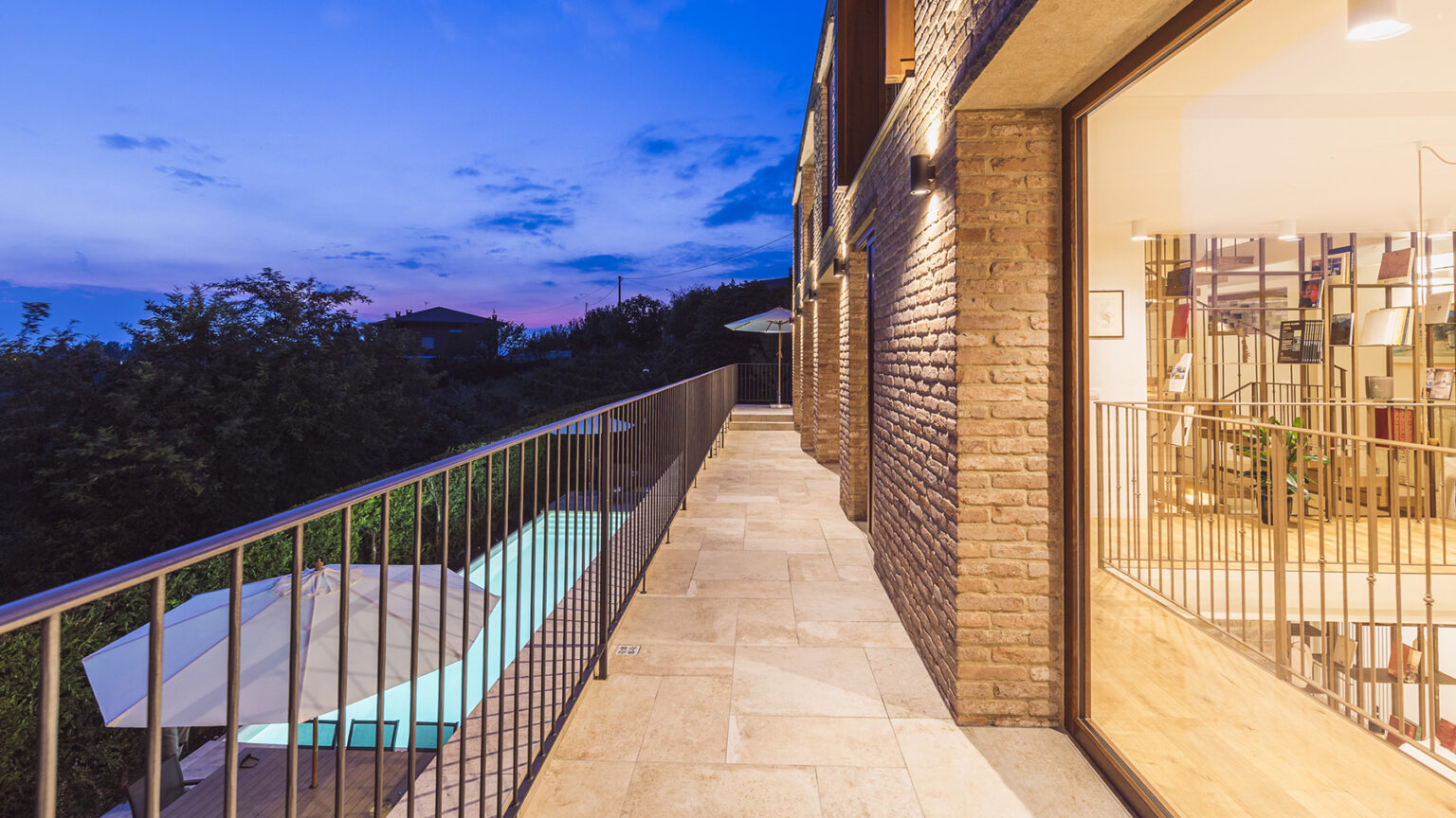 Modern balcony with a view, featuring a stone walkway, metal railing, and adjacent glass doors, set against a twilight sky. | Only on SopranoVillas