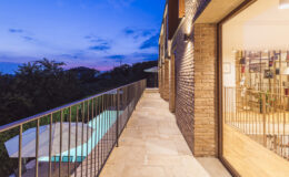 Modern balcony with a view, featuring a stone walkway, metal railing, and adjacent glass doors, set against a twilight sky.
