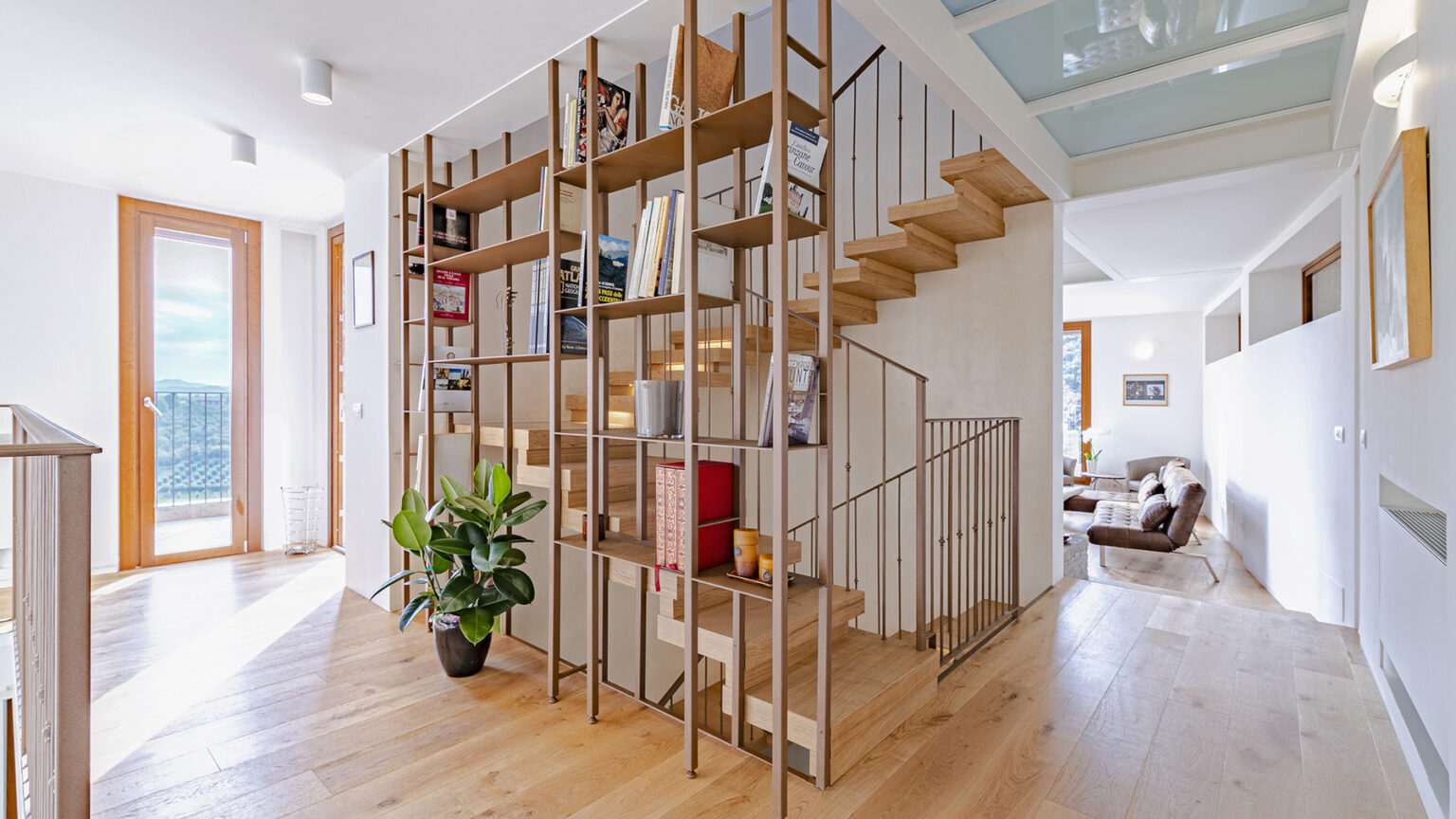 Modern interior design featuring a stylish wooden staircase with a metal railing, surrounded by natural light and contemporary decor. A potted plant adds a touch of greenery, enhancing the inviting atmosphere of the open-plan space. | Only on SopranoVillas