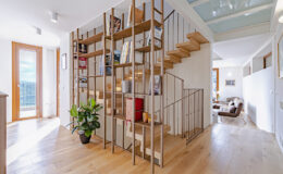 Modern interior design featuring a stylish wooden staircase with a metal railing, surrounded by natural light and contemporary decor. A potted plant adds a touch of greenery, enhancing the inviting atmosphere of the open-plan space.