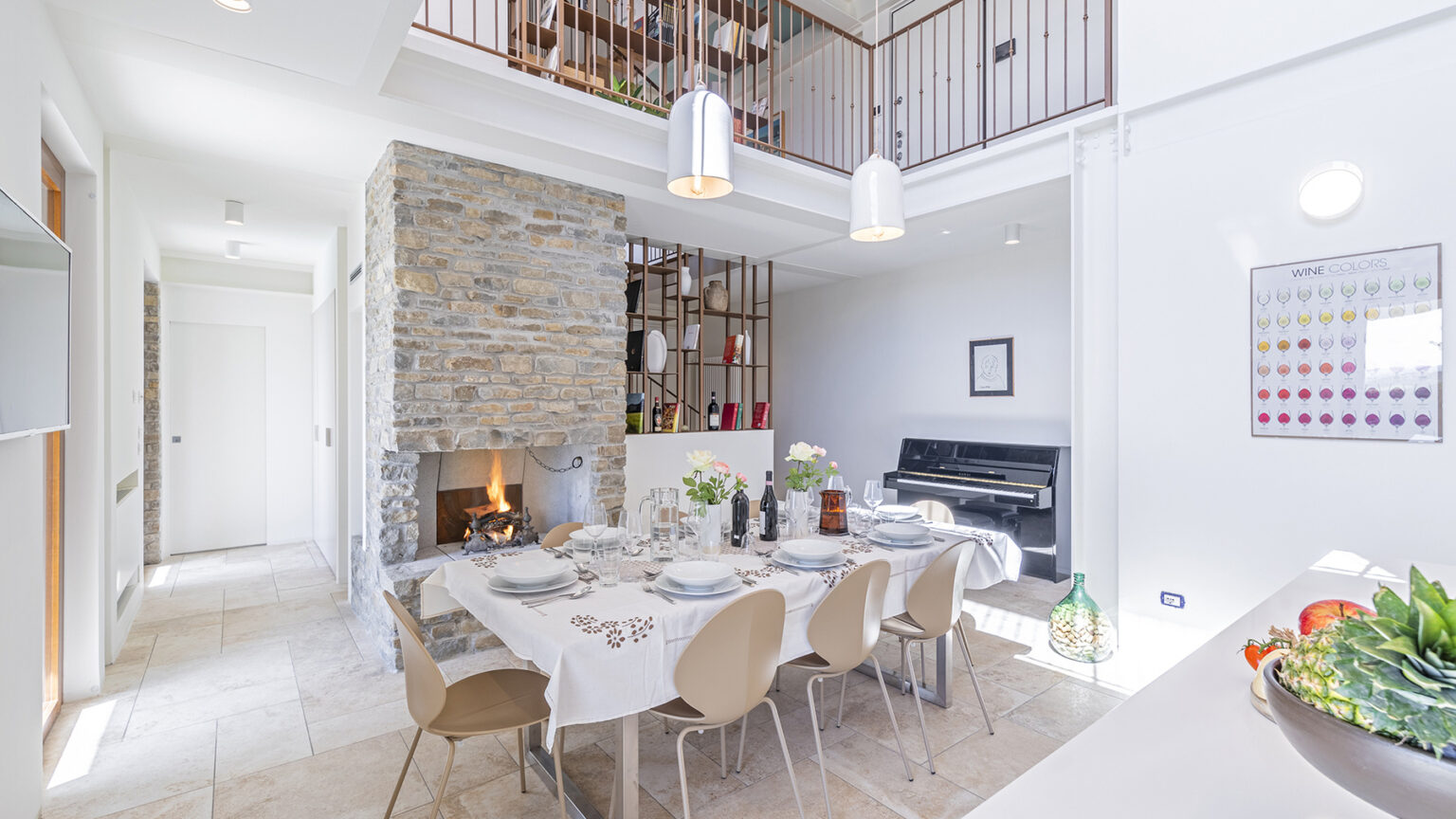 Modern dining area with a stone accent wall, featuring a large table set for a meal, stylish chairs, and an open layout that connects to a cozy living space with a fireplace. Natural light floods the room, enhancing the contemporary decor. | Only on SopranoVillas