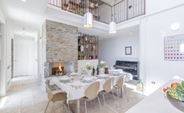 Modern dining area with a stone accent wall, featuring a large table set for a meal, stylish chairs, and an open layout that connects to a cozy living space with a fireplace. Natural light floods the room, enhancing the contemporary decor.