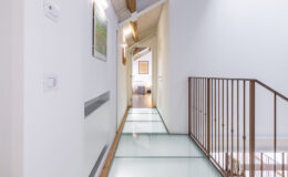 Modern interior hallway featuring a glass floor, white walls, and wooden accents, leading to a well-lit room. The design combines contemporary elements with natural light, enhancing the spacious feel of the area.