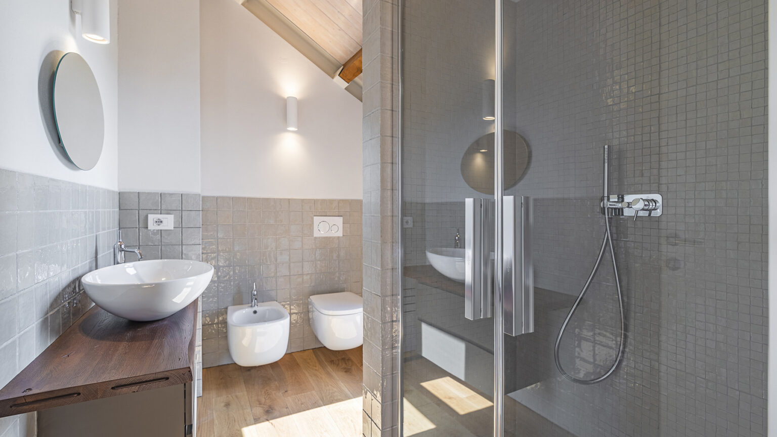 Modern bathroom featuring a glass shower enclosure, sleek vessel sink, and contemporary fixtures. The design includes neutral tile accents and wooden flooring, creating a bright and airy atmosphere. | Only on SopranoVillas