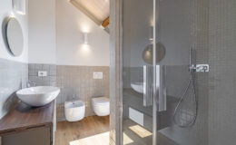 Modern bathroom featuring a glass shower enclosure, sleek vessel sink, and contemporary fixtures. The design includes neutral tile accents and wooden flooring, creating a bright and airy atmosphere.