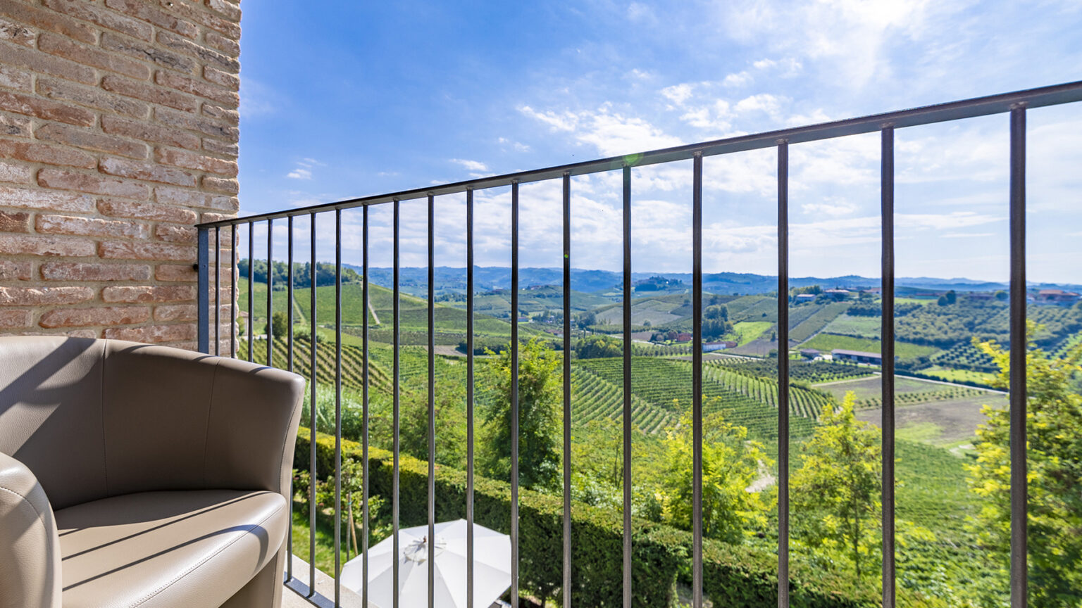Scenic view from a balcony overlooking lush green vineyards and rolling hills under a clear blue sky. | Only on SopranoVillas