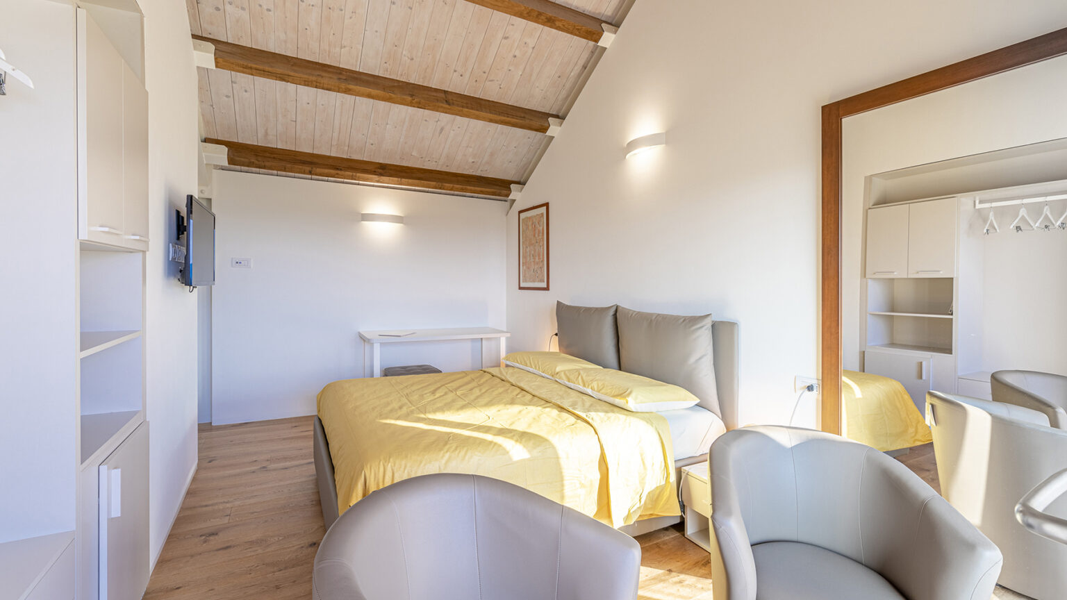 Cozy bedroom with a yellow bedspread, modern decor, and wooden beams, featuring a TV and seating area for relaxation. Ideal for a comfortable stay. | Only on SopranoVillas