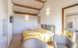 Cozy bedroom with a yellow bedspread, modern decor, and wooden beams, featuring a TV and seating area for relaxation. Ideal for a comfortable stay.