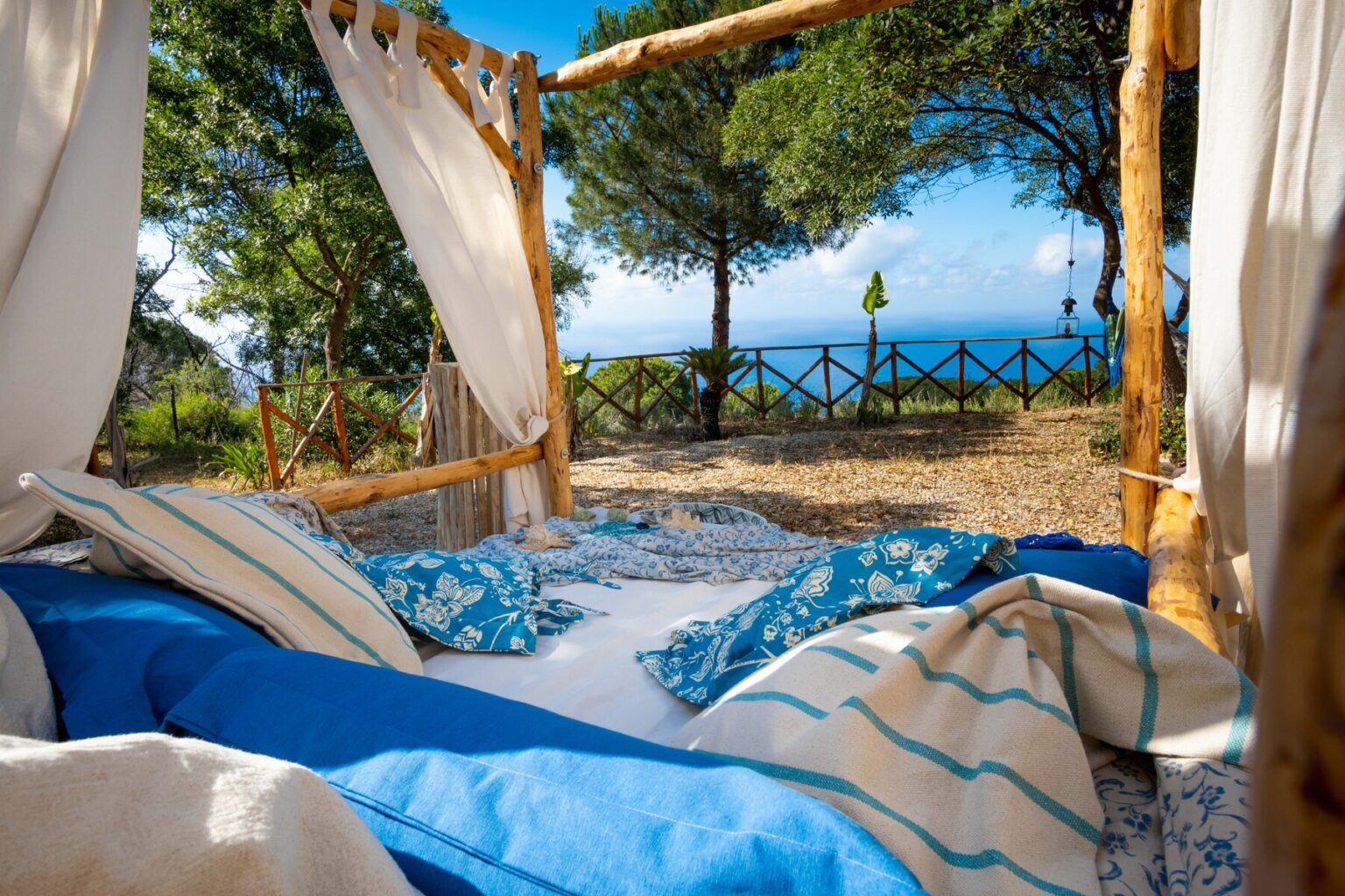 Cozy outdoor seating area with blue cushions and blankets, surrounded by trees and overlooking a serene ocean view, perfect for relaxation and enjoying nature. | Only on SopranoVillas