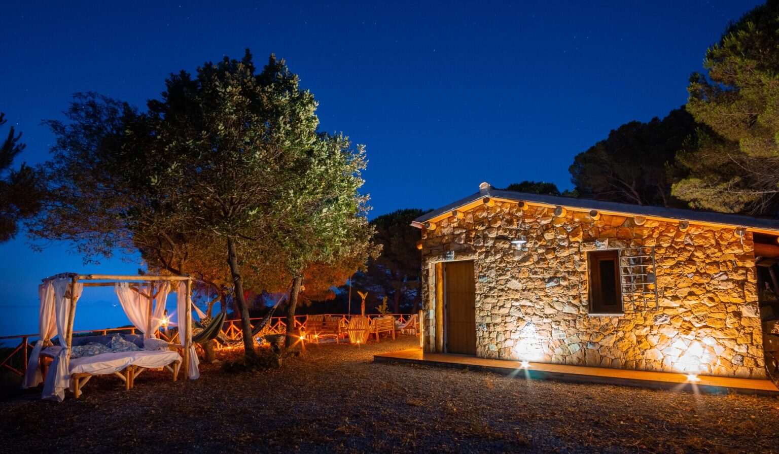 Stone cottage illuminated at night with a cozy outdoor seating area surrounded by trees, creating a tranquil atmosphere. | Only on SopranoVillas