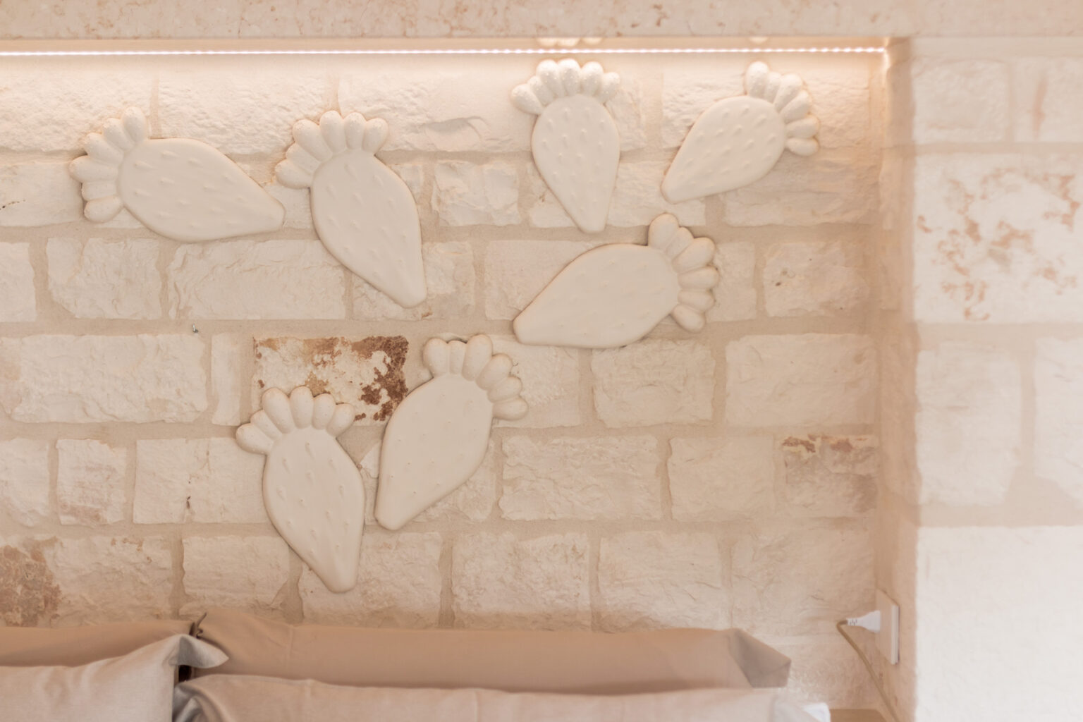 Decorative white clay wall art in the shape of leaves arranged on a rustic stone wall, enhancing the interior design of a cozy bedroom. | Only on SopranoVillas