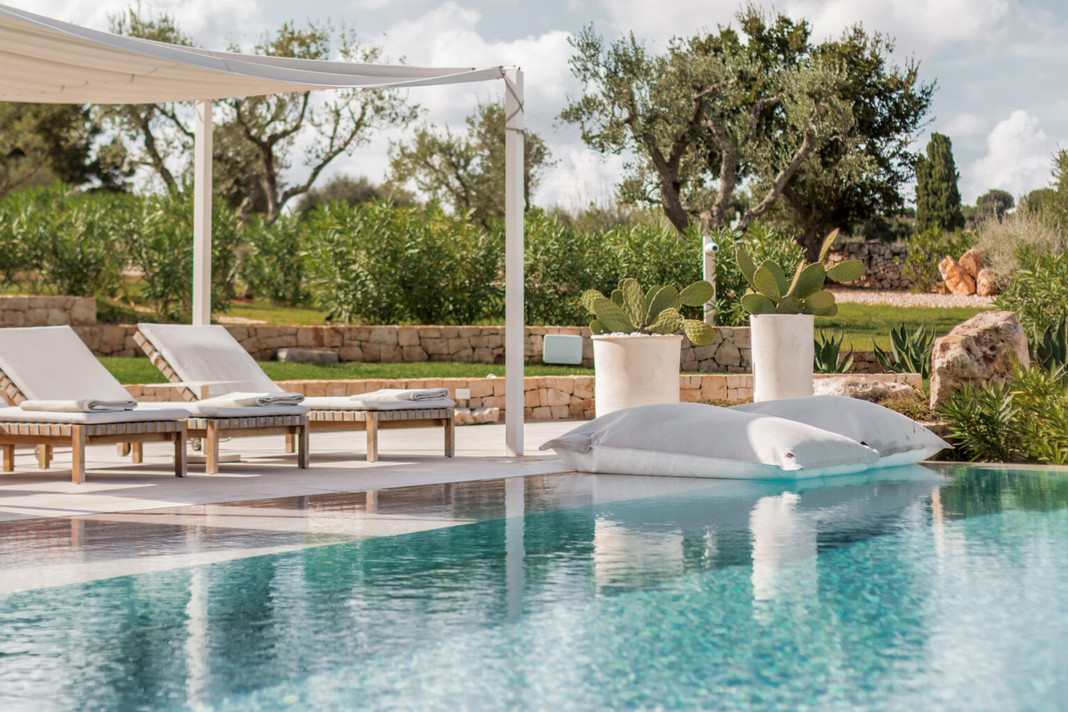 Luxurious outdoor pool area featuring stylish sun loungers, a shaded pergola, and lush greenery in the background, perfect for relaxation and leisure. | Only on SopranoVillas