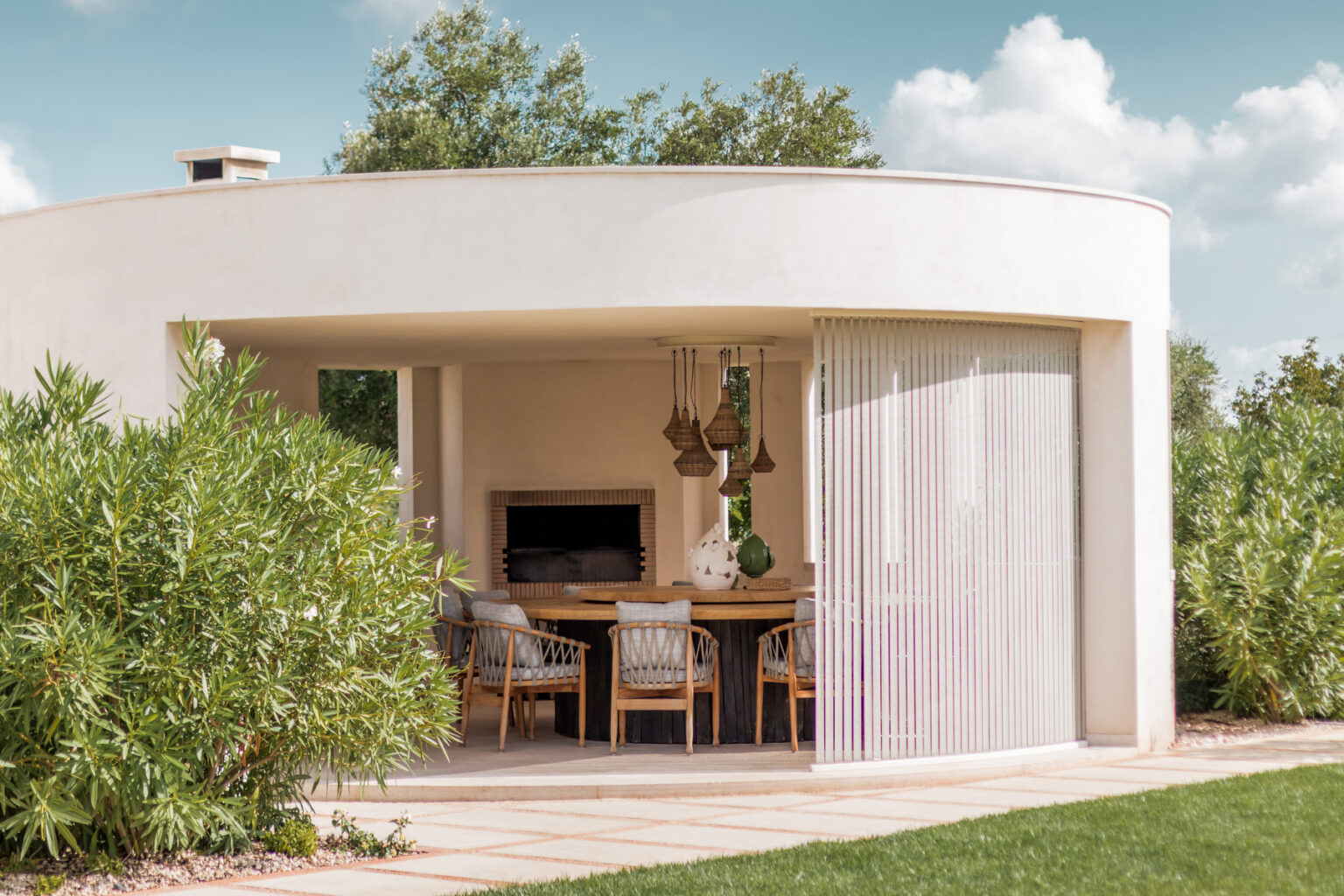 Modern outdoor dining area featuring a circular design, large windows, and elegant decor, surrounded by greenery and under a blue sky. | Only on SopranoVillas