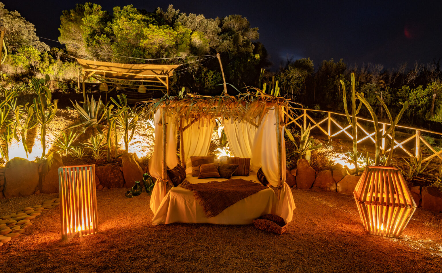 Cozy outdoor seating area with a lit canopy bed surrounded by tropical plants and decorative lanterns at night. Ideal for romantic getaways or relaxation. | Only on SopranoVillas