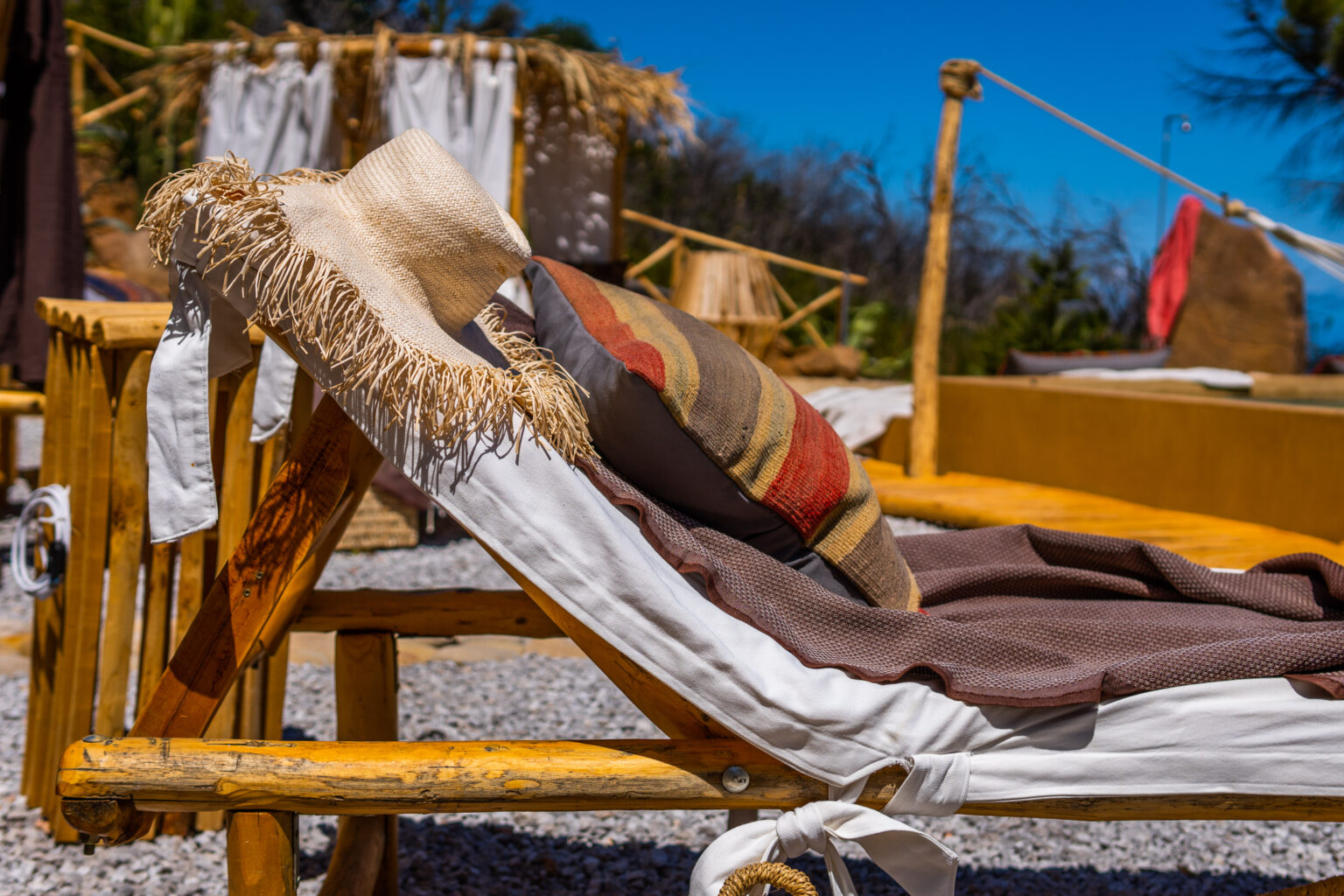 Wooden lounge chair with a straw hat and colorful blankets, set in a sunny outdoor area with a clear blue sky. Ideal for relaxation and leisure in a tranquil environment. | Only on SopranoVillas