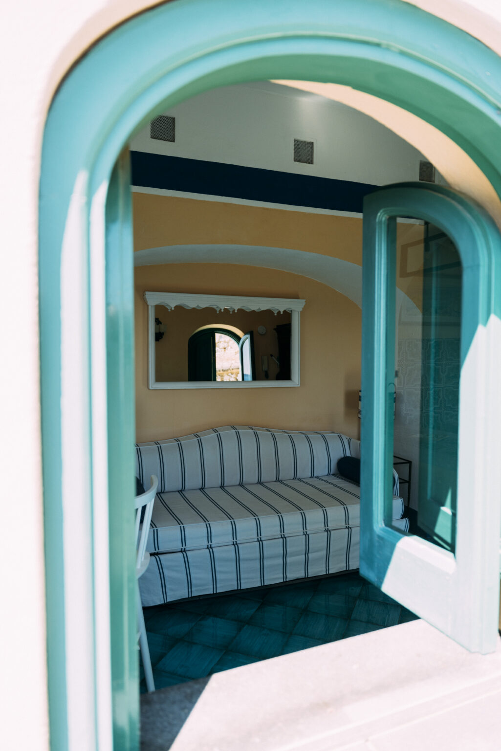 Luxurious interior of an Italian villa showcasing a cozy seating area with striped cushions, framed mirror, and arched windows, perfect for a relaxing getaway. | Only on SopranoVillas