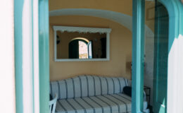 Luxurious interior of an Italian villa showcasing a cozy seating area with striped cushions, framed mirror, and arched windows, perfect for a relaxing getaway.