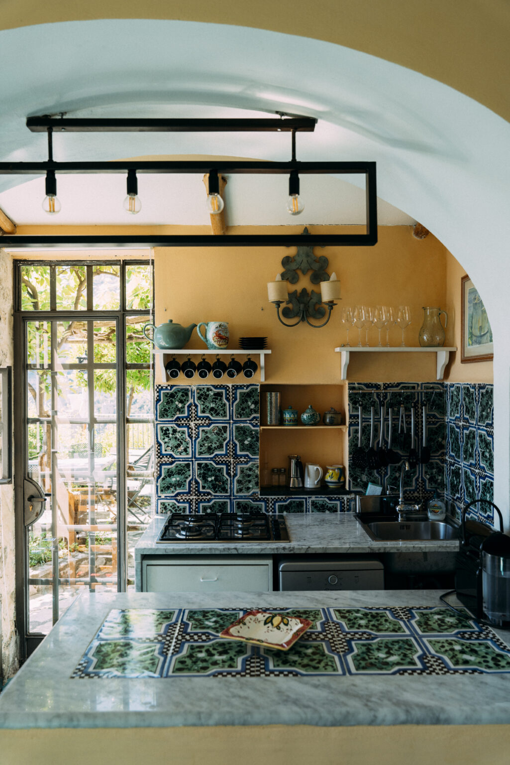 Luxury villa kitchen in Italy featuring vibrant orange walls, intricate blue tiled backsplash, and elegant decor. Ideal for gourmet cooking experiences in a picturesque setting. | Only on SopranoVillas