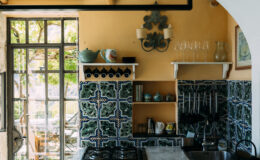 Luxury villa kitchen in Italy featuring vibrant orange walls, intricate blue tiled backsplash, and elegant decor. Ideal for gourmet cooking experiences in a picturesque setting.