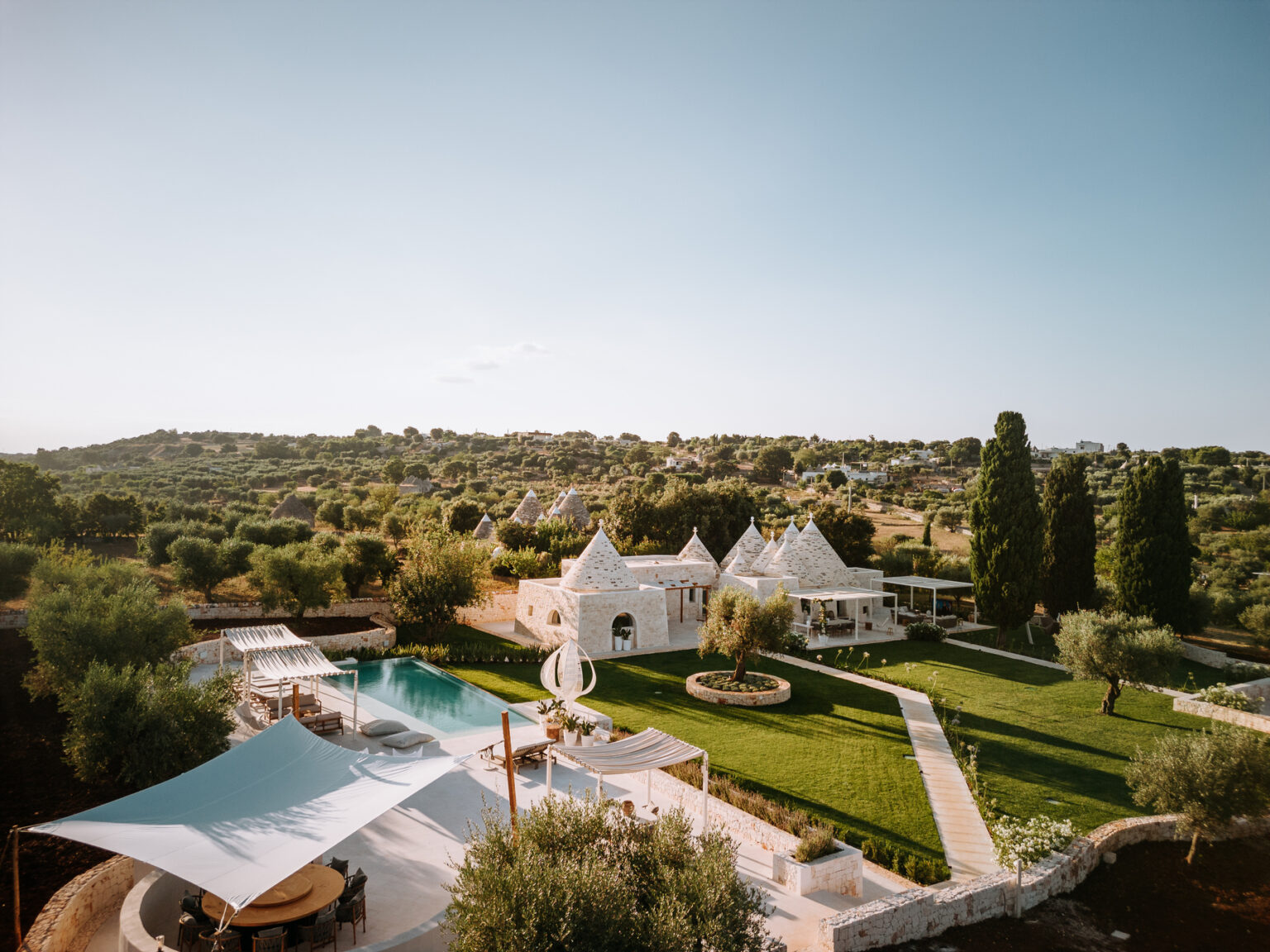 Aerial view of a luxury villa with a pool surrounded by lush greenery and olive trees, featuring traditional trullo architecture in a serene landscape. Ideal for vacation rentals and outdoor gatherings. | Only on SopranoVillas