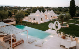 Luxurious villa with a modern pool surrounded by lush greenery, featuring traditional trullo architecture, stylish outdoor seating, and elegant landscaping in a tranquil setting.
