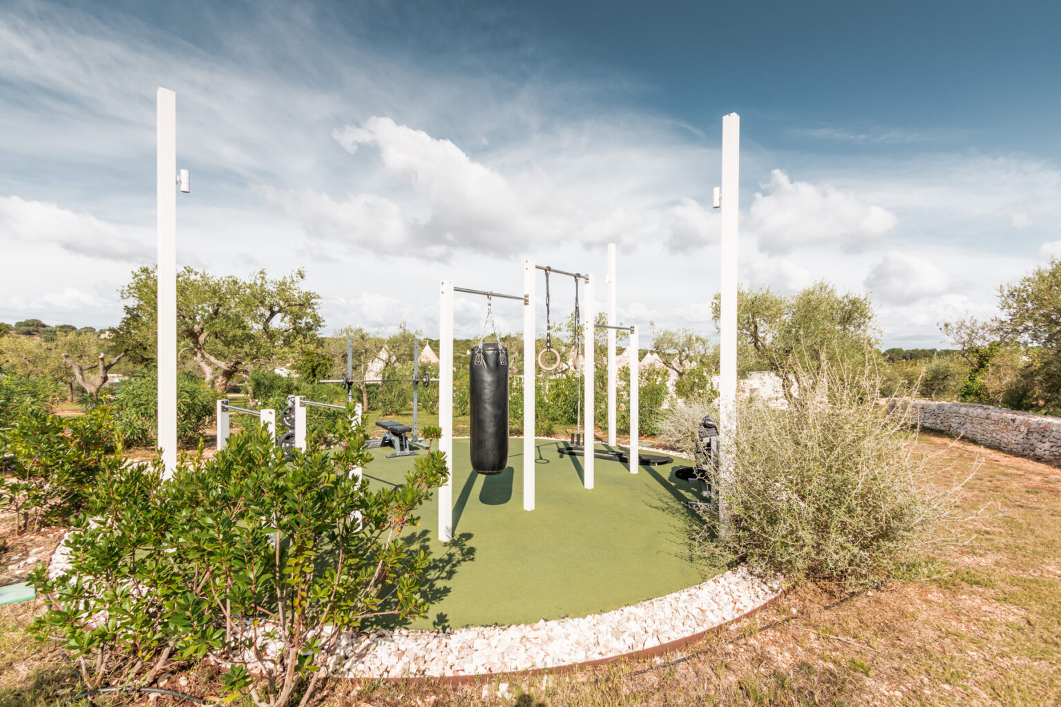 Outdoor fitness area featuring a punching bag, gymnastic rings, and exercise equipment, surrounded by greenery and scenic views. Ideal for outdoor workouts and training sessions. | Only on SopranoVillas