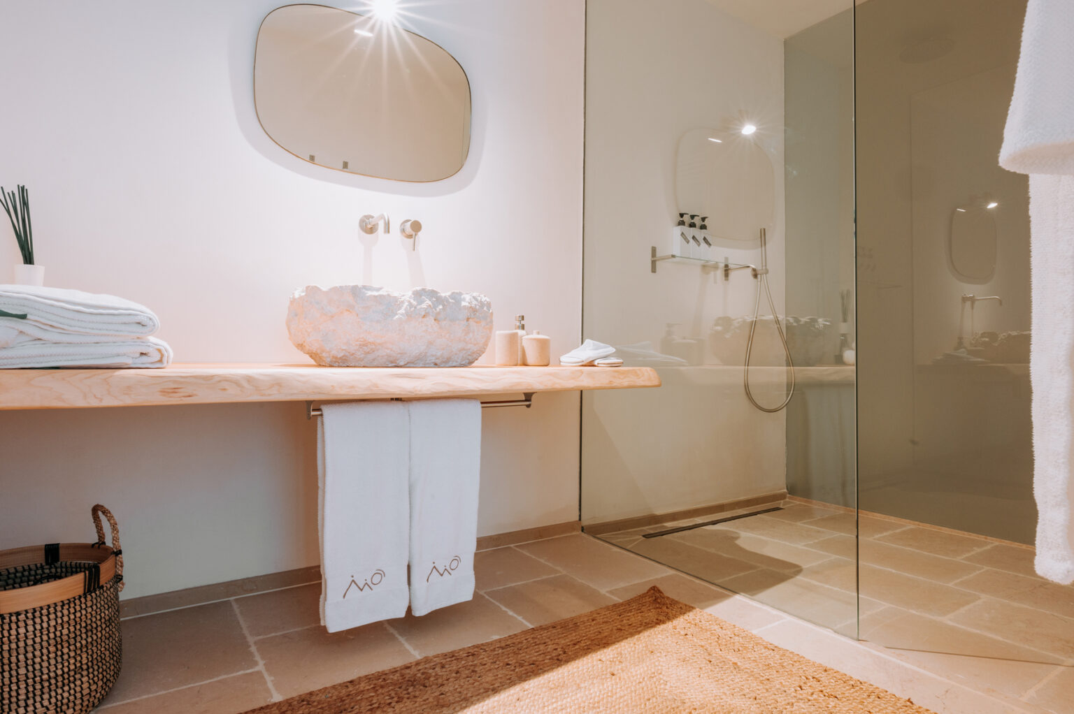 Modern bathroom interior featuring a wooden countertop with a unique sink, neatly arranged towels, and a glass shower enclosure. The design emphasizes minimalism and natural materials, creating a serene and stylish atmosphere. | Only on SopranoVillas