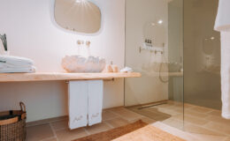 Modern bathroom interior featuring a wooden countertop with a unique sink, neatly arranged towels, and a glass shower enclosure. The design emphasizes minimalism and natural materials, creating a serene and stylish atmosphere.