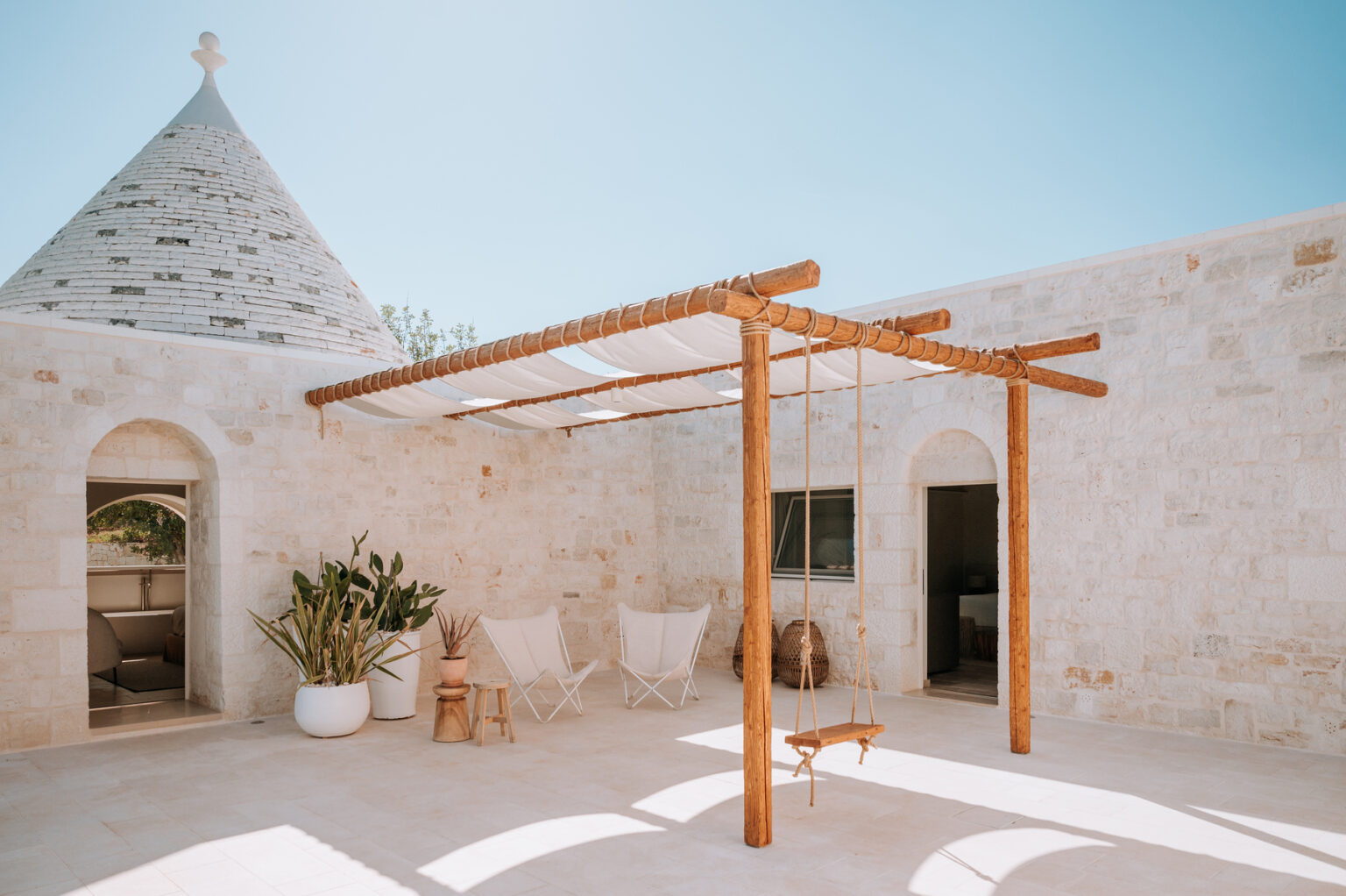 Tranquil outdoor patio featuring a wooden pergola, stone walls, and a cozy seating area, illuminated by bright sunlight, ideal for relaxation and social gatherings. | Only on SopranoVillas
