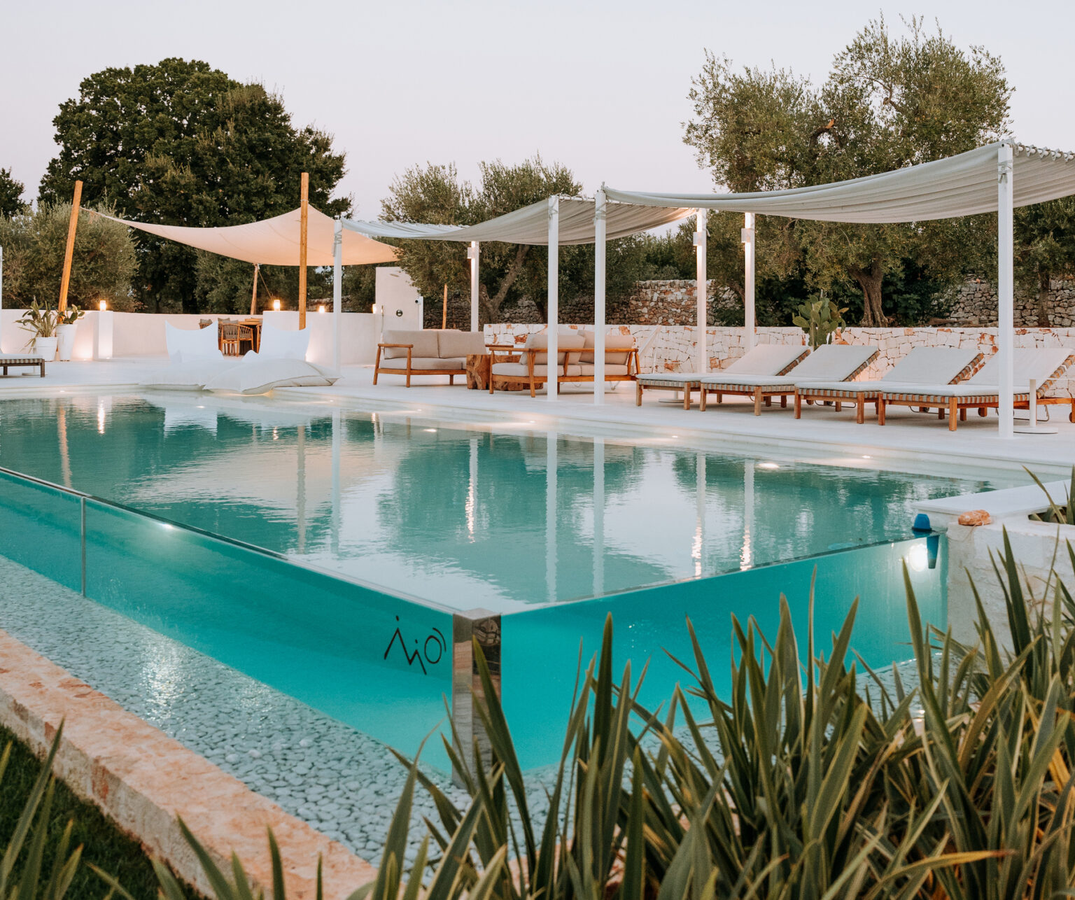 Luxury outdoor swimming pool with modern design, surrounded by lounge chairs and shaded areas, set in a serene garden environment. Ideal for relaxation and leisure activities. | Only on SopranoVillas