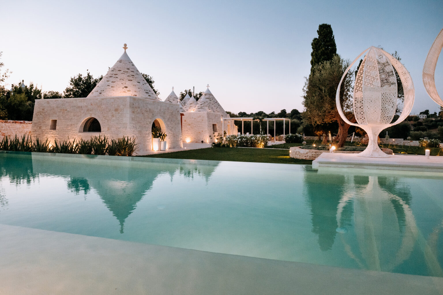 Luxury villa with trullo architecture, serene swimming pool, and landscaped gardens at dusk. Ideal for vacation rentals or destination weddings. | Only on SopranoVillas