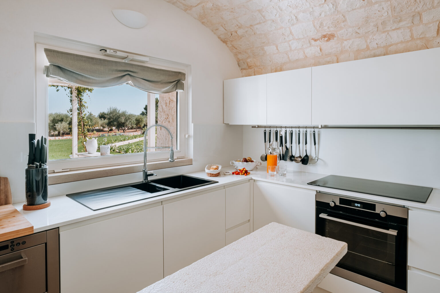 Modern kitchen with white cabinets, a large window overlooking a garden, and sleek appliances including a sink, stovetop, and oven. | Only on SopranoVillas