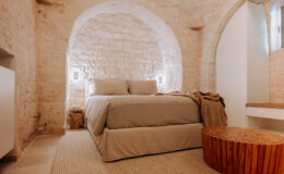 Cozy bedroom featuring a stone wall design, a comfortable bed with neutral bedding, and a rustic wooden side table, creating a warm and inviting atmosphere.
