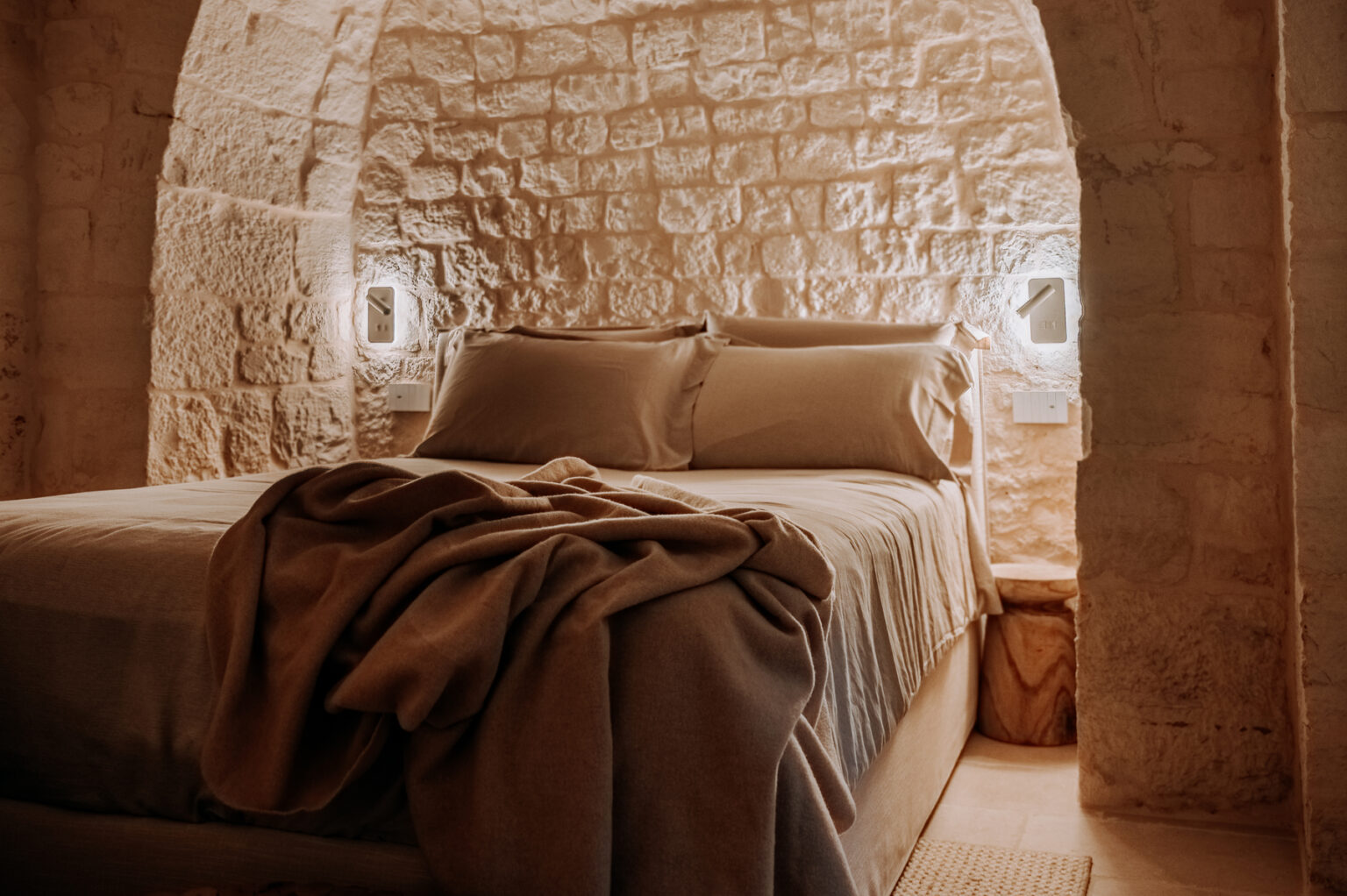 Cozy bedroom featuring a stone wall, a comfortable bed with neutral-colored bedding, and soft lighting that creates a warm atmosphere. Ideal for relaxation and a peaceful retreat. | Only on SopranoVillas